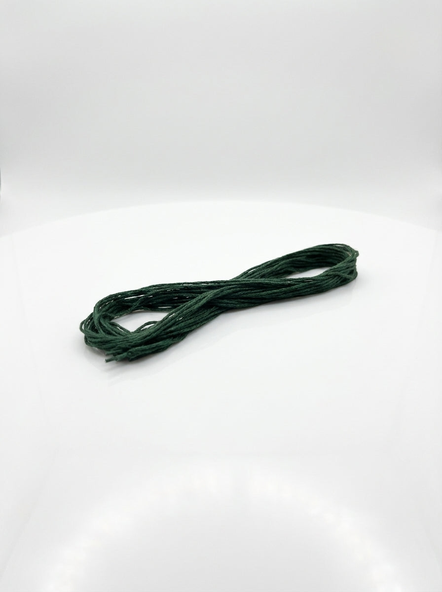 Close-up studio shot of dark blue green cotton embroidery floss skein, showing texture and color detail.