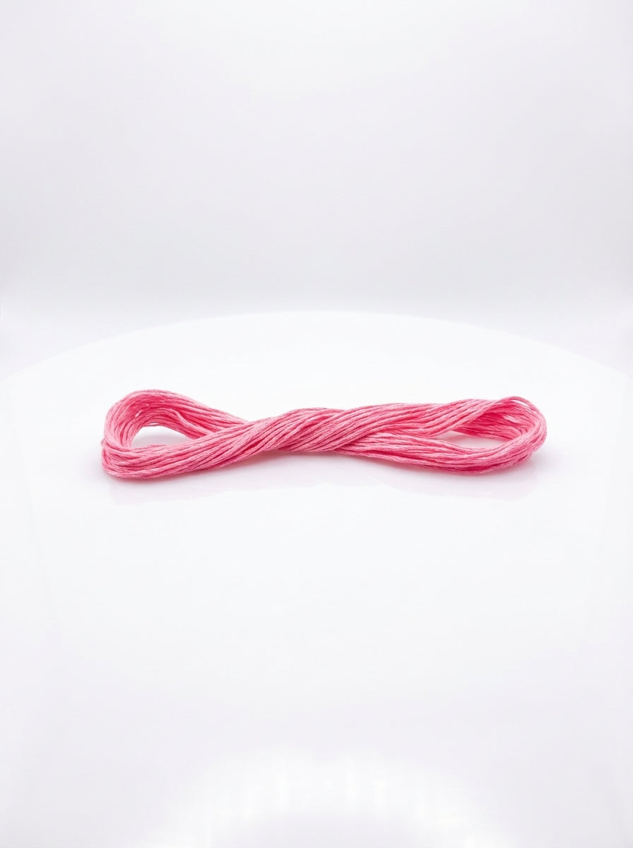 Single skein of geranium pink cotton embroidery floss, neatly wound and ready for crafting projects.