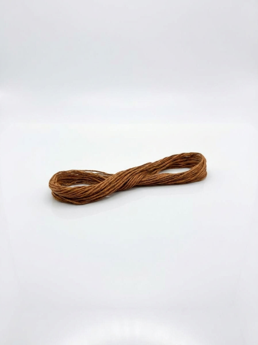 Studio shot of a golden brown cotton embroidery floss skein, wound in a figure-eight shape with a slight sheen.