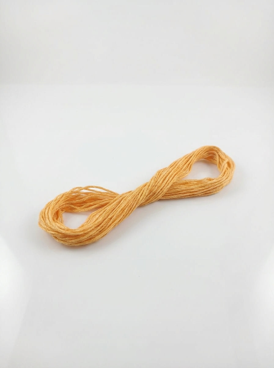 Studio shot of light gold cotton embroidery floss skein. Soft texture and subtle shimmer visible.